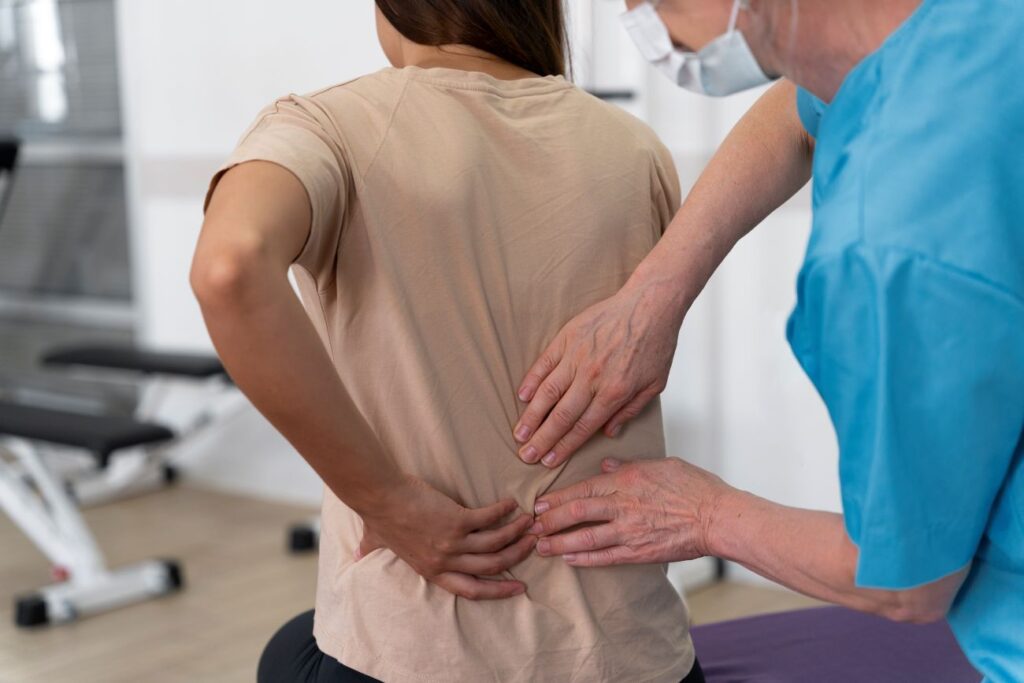 Profissional da saúde avaliando a região lombar de uma mulher com dor nas costas em ambiente clínico, durante atendimento de fisioterapia ou reabilitação.