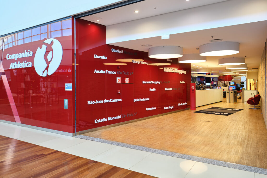 Entrada da academia Cia Athletica em Ribeirão Preto, com fachada de vidro vermelho e recepção moderna ao fundo.