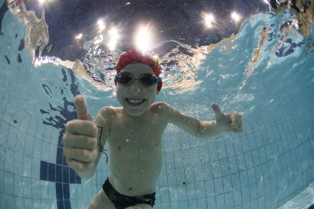 Criança no fundo da piscina sorrindo, fazendo natação.