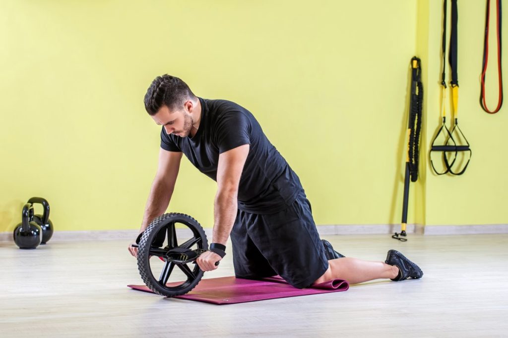 homem jovem praticando abdominal com roda no chão da academia