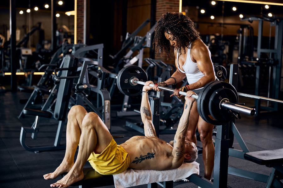 Personal trainer em academia ajuda aluno com barra com peso em treino para peito