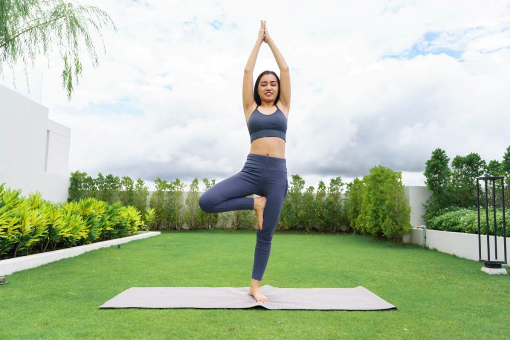 mulher realizando a postura da árvore, um dos mais conhecidos exercícios de equilíbrio no yoga.