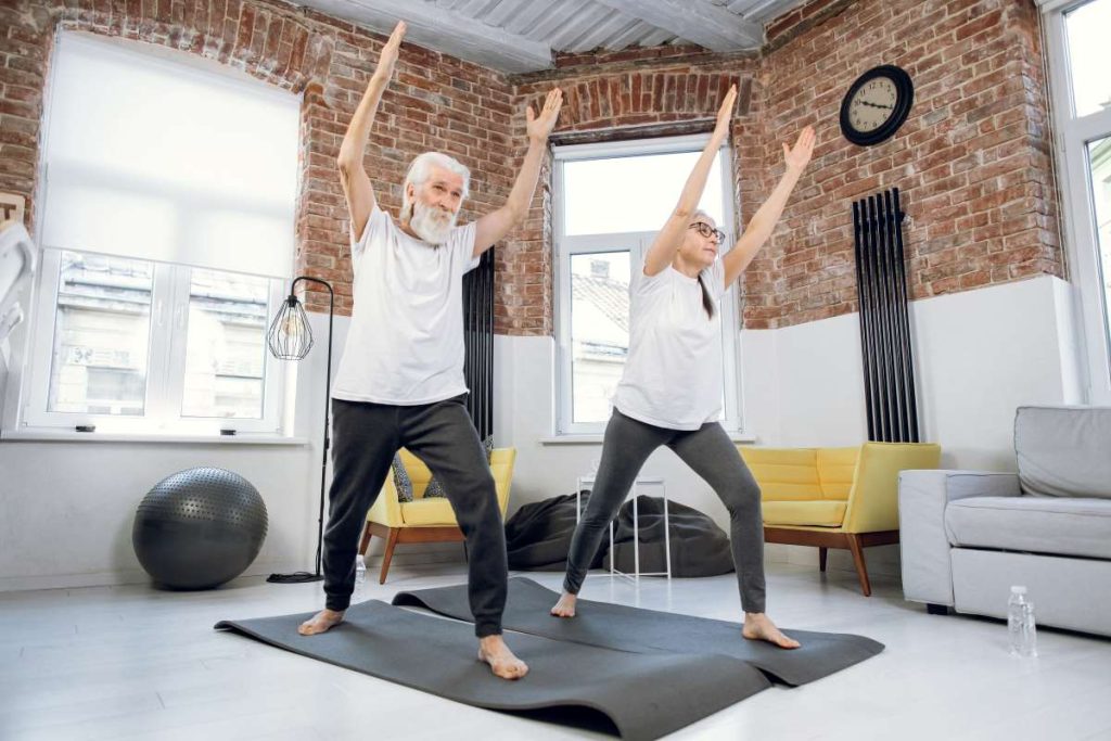 casal de idosos praticando exercícios de equilíbrio em uma sala iluminada.