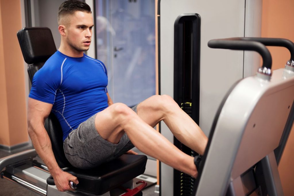 homem realizando o exercício leg press horizontal em uma academia.