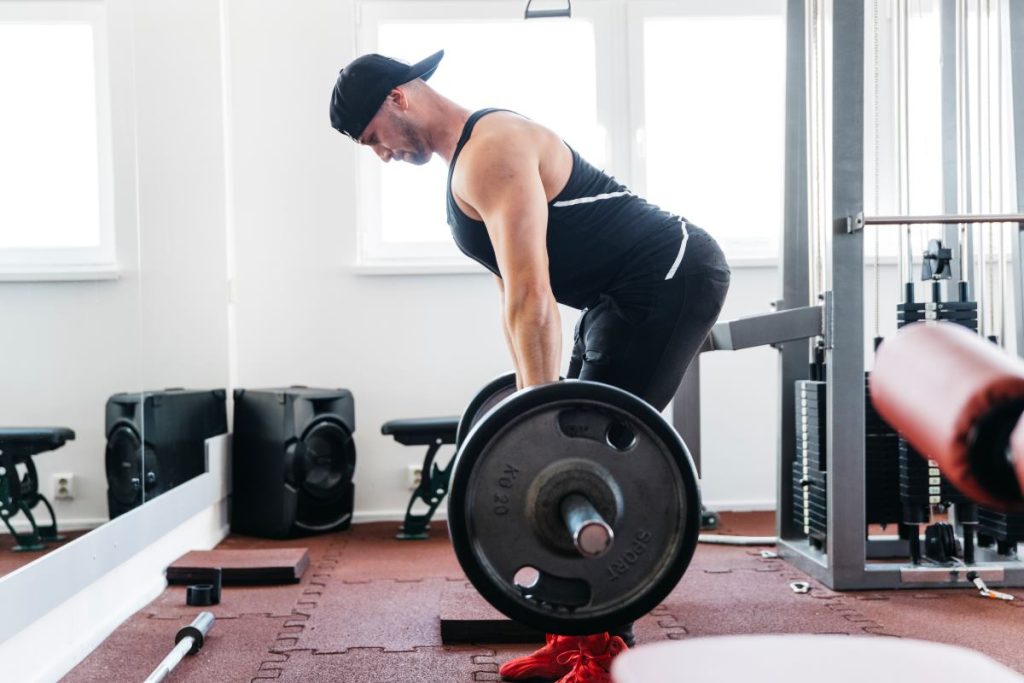 homem está realizando o exercício stiff, focado na região lombar, em uma academia. 