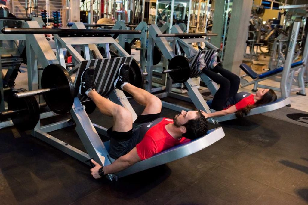 duas pessoas realizando treino de pernas na academia utilizando o aparelho leg 45°