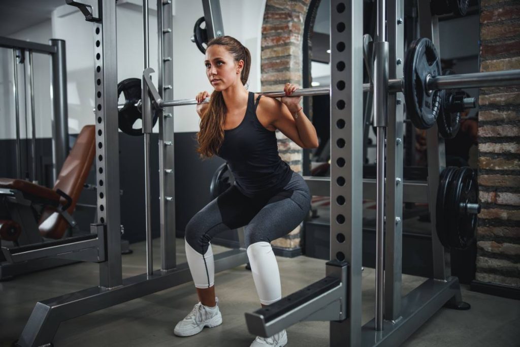 mulher realizando um exercício de agachamento com ênfase na musculatura posterior da coxa.