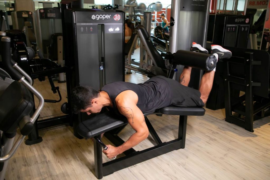 homem realizando um exercício na mesa flexora, com ênfase na musculatura posterior da coxa.