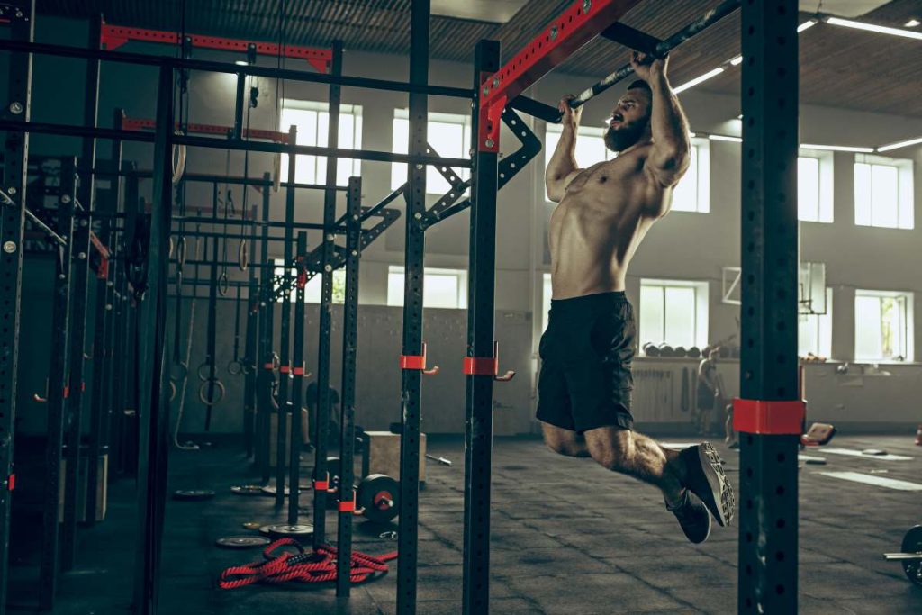 homem musculoso realizando um exercício de treino de costas em uma barra fixa em uma academia