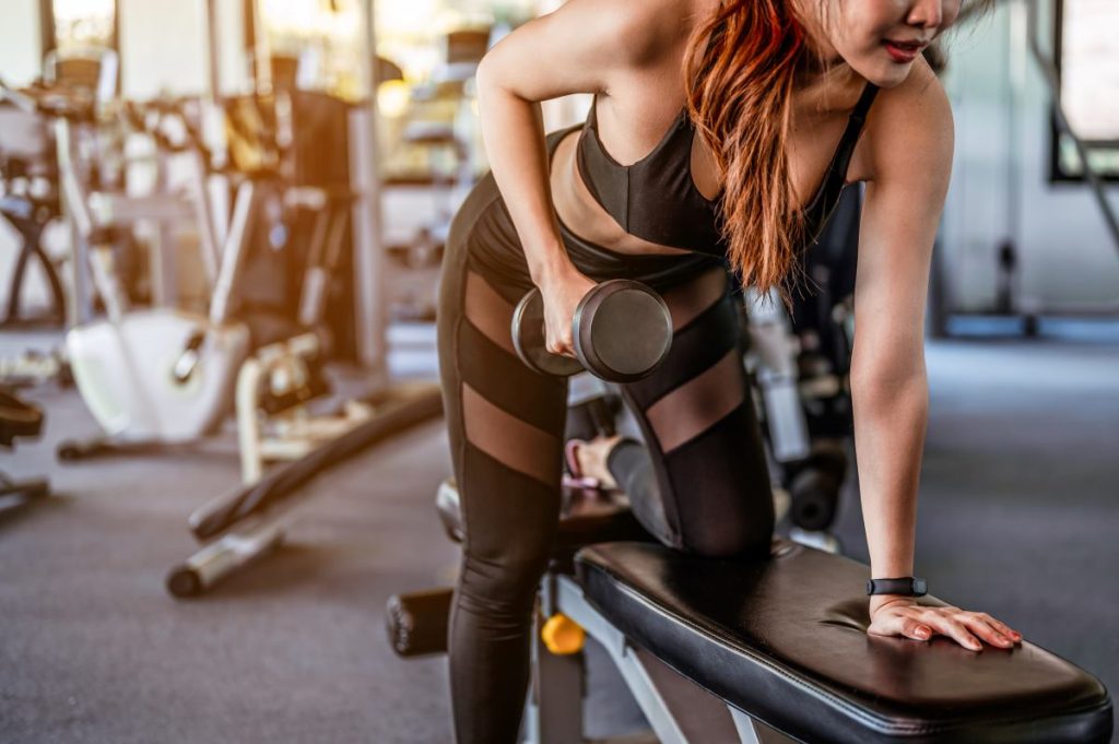 mulher realizando um exercício de remada unilateral em um equipamento de musculação.