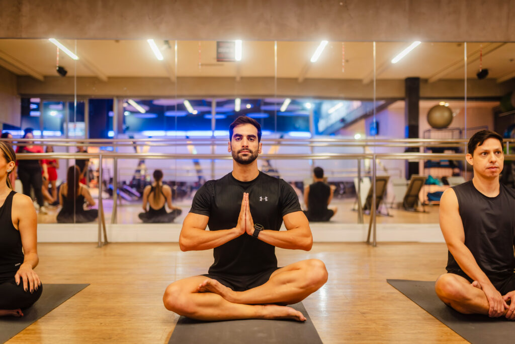 Homem sentado em posição de meditação durante aula na Cia Athletica RAO, com outras pessoas ao redor praticando Yoga.