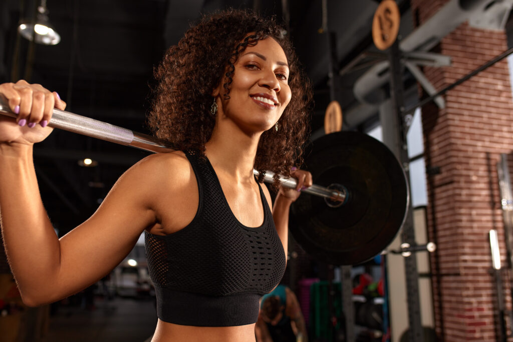 Benefícios da musculação: mais saúde, força e qualidade de vida Mulher praticando musculação com barra apoiada nos ombros durante treino de força em academia.